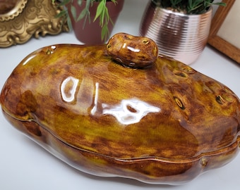 May include: A brown ceramic potato-shaped dish with a lid. The dish has a glossy finish and a realistic potato texture.