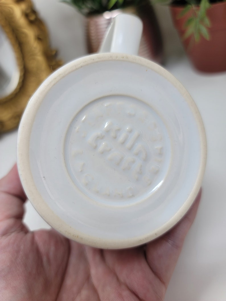 May include: White ceramic mug with a white logo that reads "Griffin  Paris" on the bottom.