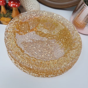 Peut inclure: Un ensemble de quatre assiettes plates en verre ton or avec une surface texturée. Les assiettes sont empilées les unes sur les autres.