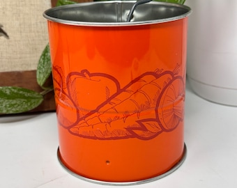 May include: Orange metal grater with a black handle. The grater has a design of carrots, apples, and other vegetables.