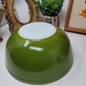 Puede incluir: Un cuenco mezclador verde vintage con interior blanco. El cuenco tiene forma redondeada y acabado brillante. Probablemente está hecho de vidrio o material similar. Un artículo de cocina clásico.