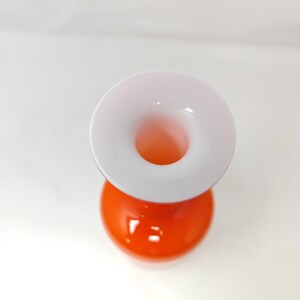 May include: A modern, two-toned vase with a spherical orange base and a white, flared top. The vase has a smooth, glossy finish and a circular opening. The design is simple and elegant, suitable for displaying flowers or as a decorative piece.