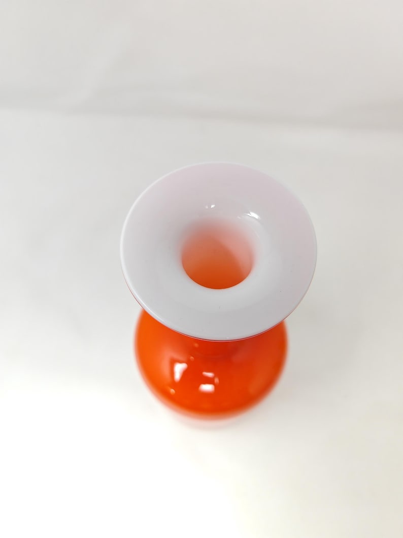 May include: A modern, two-toned vase with a spherical orange base and a white, flared top. The vase has a smooth, glossy finish and a circular opening. The design is simple and elegant, suitable for displaying flowers or as a decorative piece.
