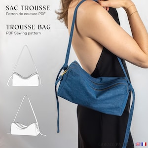 Könnte beinhalten: Eine blaue Jeansstoff-Umhängetasche mit rechteckiger Form und zwei Reißverschlussfächern. Die Tasche hat einen langen, verstellbaren Riemen. Auf der linken Seite steht "SAC TROUSSE" und "TROUSSE BAG".