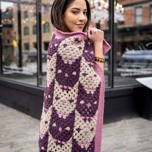 May include: A crochet blanket featuring a repeating pattern of owl motifs in shades of dark purple, light beige, and soft pink. The blanket has a solid pink crocheted border along the edge and is constructed from interconnected square blocks.
