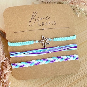 May include: A set of three bracelets on a brown card labelled Bini Crafts. The top bracelet is a light blue knotted cord with a silver starfish charm. The middle consists of layered light blue, purple, and white strings. The bottom is a braided cord.