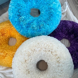 May include: Four handmade paper wreaths in different colors: yellow, blue, white, and purple. The wreaths are made of paper that has been curled and layered to create a fluffy, textured look.