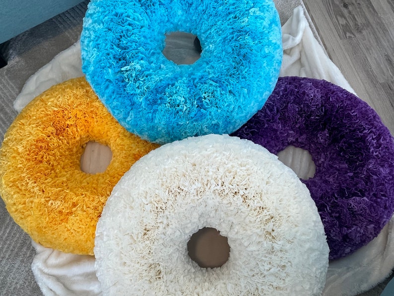 May include: Four handmade paper wreaths in different colors: yellow, blue, white, and purple. The wreaths are made of paper that has been curled and layered to create a fluffy, textured look.