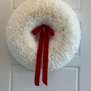 May include: A white coffee filter wreath with a red ribbon bow. The wreath is hanging on a white door.