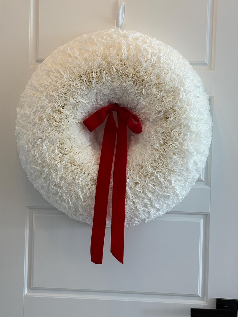 May include: A white coffee filter wreath with a red ribbon bow. The wreath is hanging on a white door.