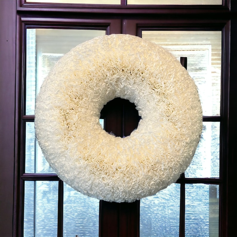 May include: A white paper coffee filter wreath hanging on a dark brown wooden door.