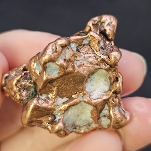May include: A close-up of a copper mineral specimen. The specimen has a rough, textured surface with a mix of copper and light blue-green hues. The copper appears to be in a natural, unpolished state.