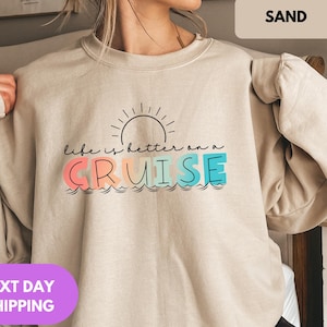 May include: A beige sweatshirt with a graphic print that says "Life is better on a cruise" with a sun and waves. The text is in black and the sun and waves are in rainbow colors.