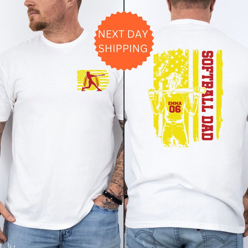 May include: White t-shirt with a softball player graphic on the front and a yellow and red American flag with the text "Softball Dad" on the back. The player is holding a bat and has the name "Emma" and number "06" on her jersey.