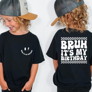 May include: Black t-shirt with a white smiley face and the text "Bruh it's my birthday" on the front. The back of the shirt has a white checkered border with the text "Bruh it's my birthday" in white.