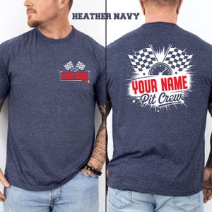 May include: Heather navy t-shirt with a racing theme. The front features a small design with checkered flags and the text "YOUR NAME". The back displays a larger design with checkered flags, a speedometer, and the text "YOUR NAME Pit Crew".