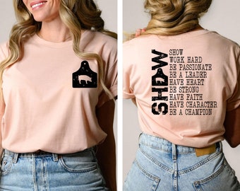 May include: A pink t-shirt with a black pig silhouette on the left side and the text "SHOW WORK HARD BE PASSIONATE BE A LEADER HAVE HEART BE STRONG HAVE FAITH HAVE CHARACTER BE A CHAMPION" on the right side.