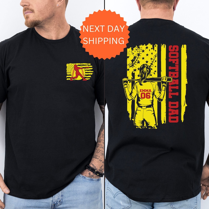 May include: Black t-shirt with a yellow and red softball player graphic on the front and a yellow and red American flag with the text "Softball Dad" on the back. The player is holding a bat and has the name "Emma" and number "06" on her jersey.