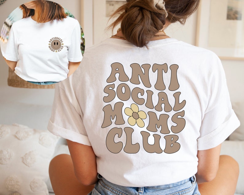 May include: White t-shirt with brown text that reads "Anti Social Moms Club" with a yellow daisy in the middle of the word "Moms".