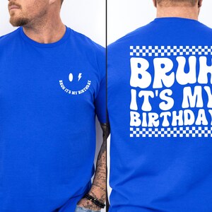 May include: A royal blue t-shirt with a white smiley face with a lightning bolt for an eye and the text "Bruh it's my birthday" on the front. The back of the shirt has the text "Bruh it's my birthday" in a retro font with a checkered border.