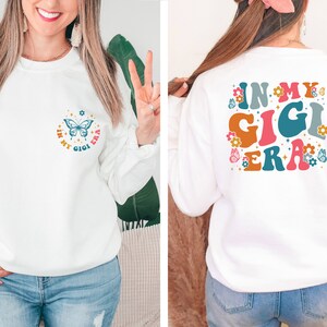 May include: White sweatshirt with a butterfly and the text "In My Gigi Era" on the front and the text "In My Gigi Era" in large, colorful letters on the back.