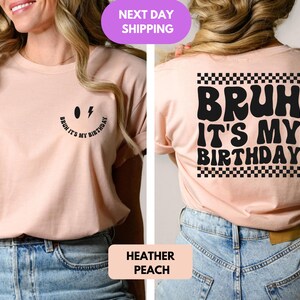 May include: A light pink t-shirt with a black smiley face and the text "Bruh it's my birthday" on the front. The back of the shirt has the text "Bruh it's my birthday" in a retro font with a black and white checkered pattern.