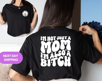 May include: Black t-shirt with white text on the back that reads "I'M NOT JUST A MOM I'M ALSO A BITCH." The front of the shirt has a small graphic with the text "Just a Mom in a world full of bitches."