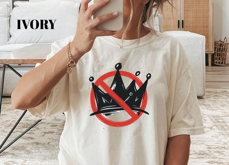 Pode incluir: Camiseta cor marfim com um desenho de coroa preta riscada com um c&iacute;rculo vermelho. A camiseta gr&aacute;fica tem um ajuste folgado e mangas curtas. A palavra "IVORY" &eacute; impressa no topo.