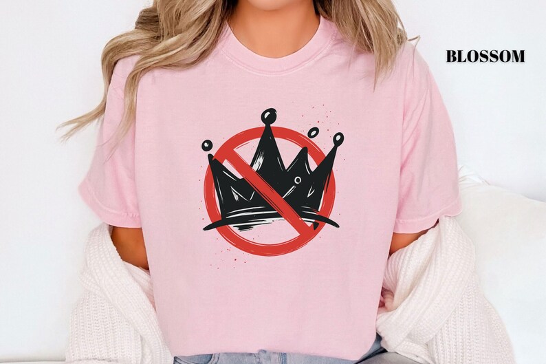 Pode incluir: Camiseta rosa claro com um desenho de coroa preta dentro de um c&iacute;rculo vermelho com uma linha diagonal. A palavra "BLOSSOM" est&aacute; impressa em preto no canto superior direito. O design &eacute; uma declara&ccedil;&atilde;o.