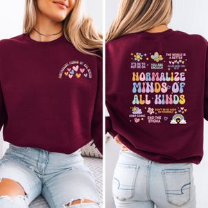 May include: Burgundy sweatshirt with the text "Normalize Minds of All Kinds" and colorful heart graphics. The back of the sweatshirt features the same text with additional phrases and graphics, including a rainbow and flowers.