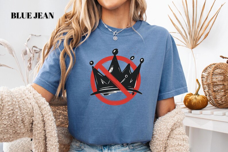 Pode incluir: Camiseta azul jeans com um gr&aacute;fico de uma coroa preta riscada por um c&iacute;rculo vermelho e uma linha diagonal. O texto "BLUE JEAN" est&aacute; no canto superior esquerdo.