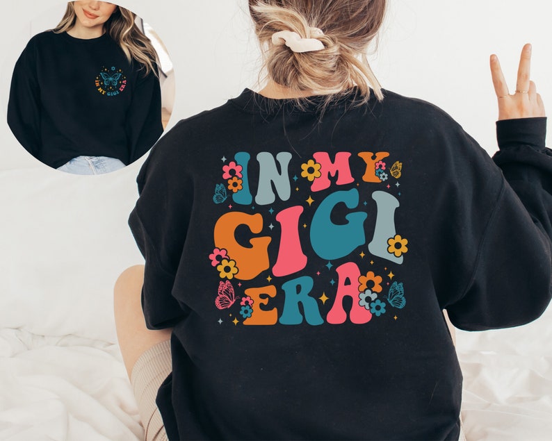 May include: Black sweatshirt with a colorful graphic design that says "In My Gigi Era" with flowers and butterflies.