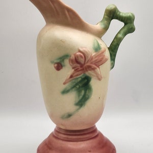 May include: A vintage ceramic pitcher with a pink and green floral design. The pitcher has a wide, flared spout and a handle shaped like a branch. The base is a wide, rounded shape with a pink glaze.
