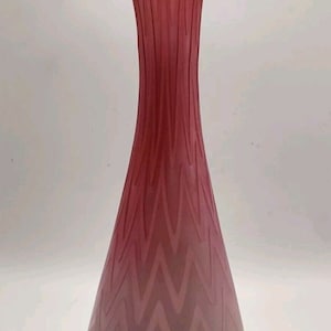 May include: A tall, pink glass vase with a ruffled top and a wavy, chevron pattern. The vase is made of glass and has a clear, translucent finish.