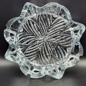 Puede incluir: Un cenicero de vidrio transparente con un diseño de estrella. El cenicero tiene una superficie texturizada y un borde festoneado.