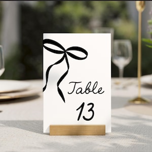 May include: White table number card with a black ribbon bow and the text "Table 13".