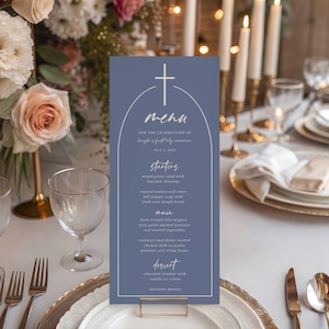 Può includere: Un menu blu con un design a croce, con un menu per una celebrazione. Il menu include antipasti, piatti principali e dessert. La carta è posta su un tavolo con composizioni floreali, candele e stoviglie eleganti.