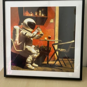 May include: A painting of an astronaut sitting at a table in a cafe, wearing a white spacesuit and holding a cup. The cafe is painted in warm colors with a red wall and a dark green plant in the background.