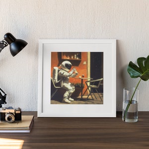 May include: A framed print of a painting depicting an astronaut sitting at a table outside a building, holding a cup. The astronaut is wearing a white spacesuit with a backpack. The building is painted orange and has a window with a view of stars. The table is brown and has a glass of liquid on it. There is a green plant in a pot on the table.