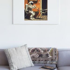 May include: A white astronaut in a spacesuit sits at a table with a glass of liquid in their hand. The astronaut is sitting in a chair with a red and orange wall behind them.