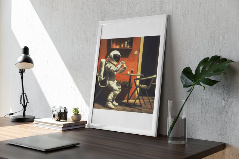May include: A framed illustration of an astronaut sitting at a table outside, wearing a white spacesuit and holding a glass of liquid. The astronaut is sitting at a table with a red wall and a green plant behind them.