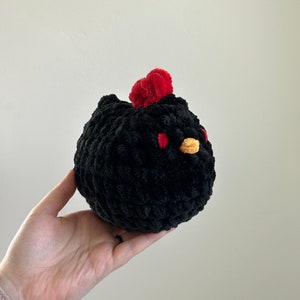 May include: Black crocheted chicken plush toy with red and yellow accents.