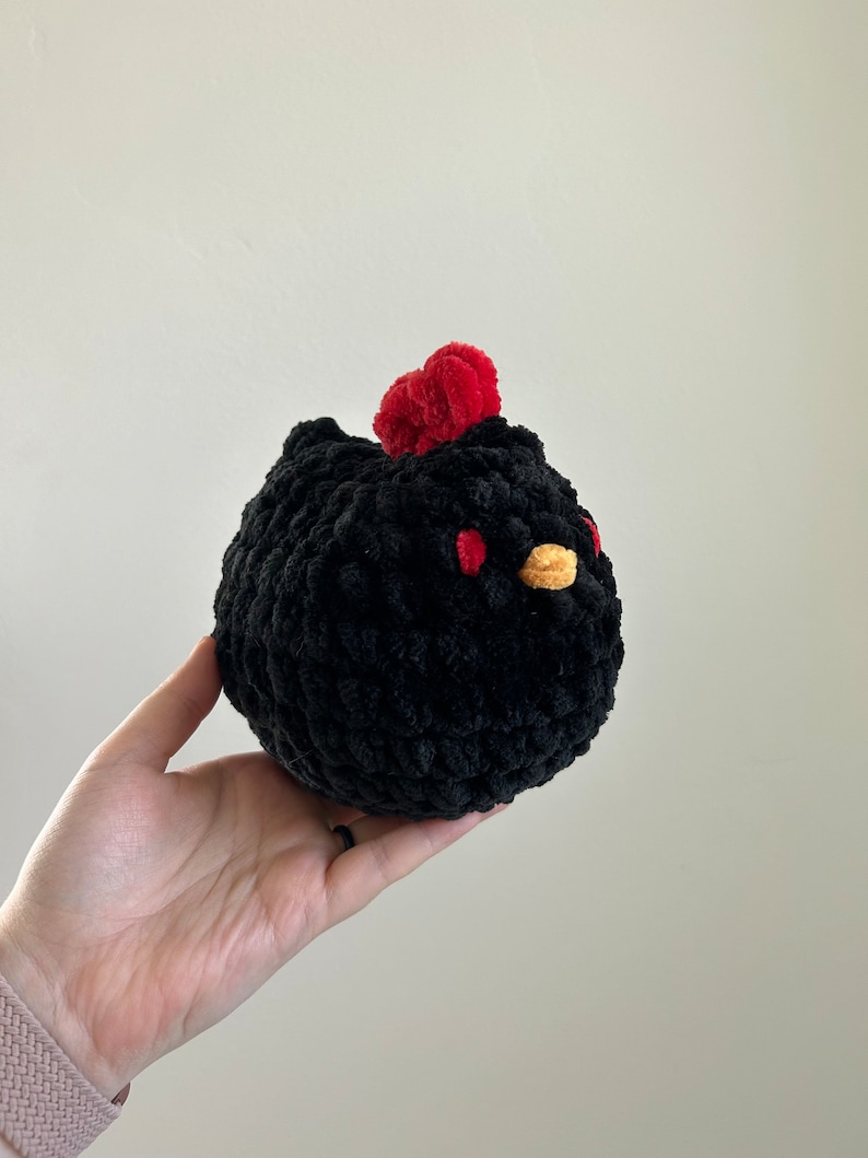 May include: Black crocheted chicken plush toy with red and yellow accents.