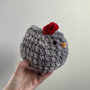 May include: A gray crocheted chicken toy with a red comb and a yellow beak.