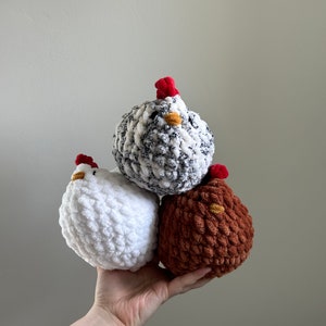 May include: Three crocheted chicken toys. One is white, one is brown, and one is black and white.