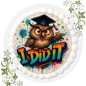 Könnte beinhalten: Ein runder Kuchen, verziert mit weißem Zuckerguss und einem farbenfrohen Bild. Das Bild zeigt eine Cartoon-Eule mit Doktorhut und den Worten "I DID IT" im Graffiti-Stil. Die Eule ist braun mit großen Augen, vor einem Hintergrund aus bunten Farbspritzern.