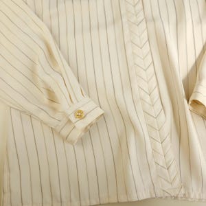 May include: A white button-down shirt with thin black stripes and a decorative chevron detail down the front.