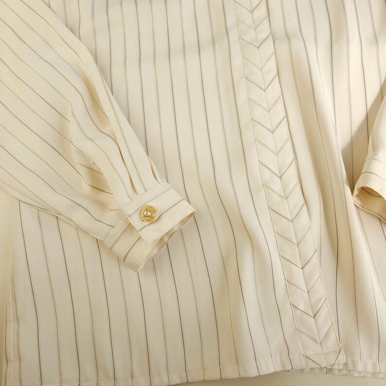 May include: A white button-down shirt with thin black stripes and a decorative chevron detail down the front.