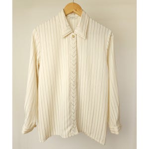 May include: A white long-sleeved button-down shirt with thin black stripes. The shirt has a pointed collar and a chevron-shaped detail down the front.