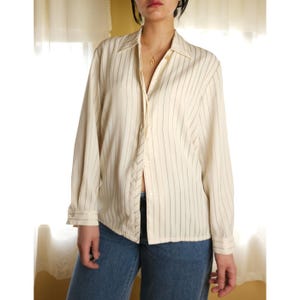 May include: A white long-sleeved button-down shirt with thin black stripes. The shirt has a classic collar and a relaxed fit.